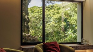 A room with a large window offering a view of dense greenery outside. - Solar dos Cantos Botanic House and Garden (Ponta Delgada)