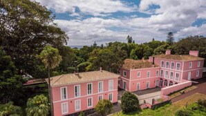 A pink building with multiple windows and a tiled roof, surrounded by greenery. - Solar dos Cantos Botanic House and Garden (Ponta Delgada)