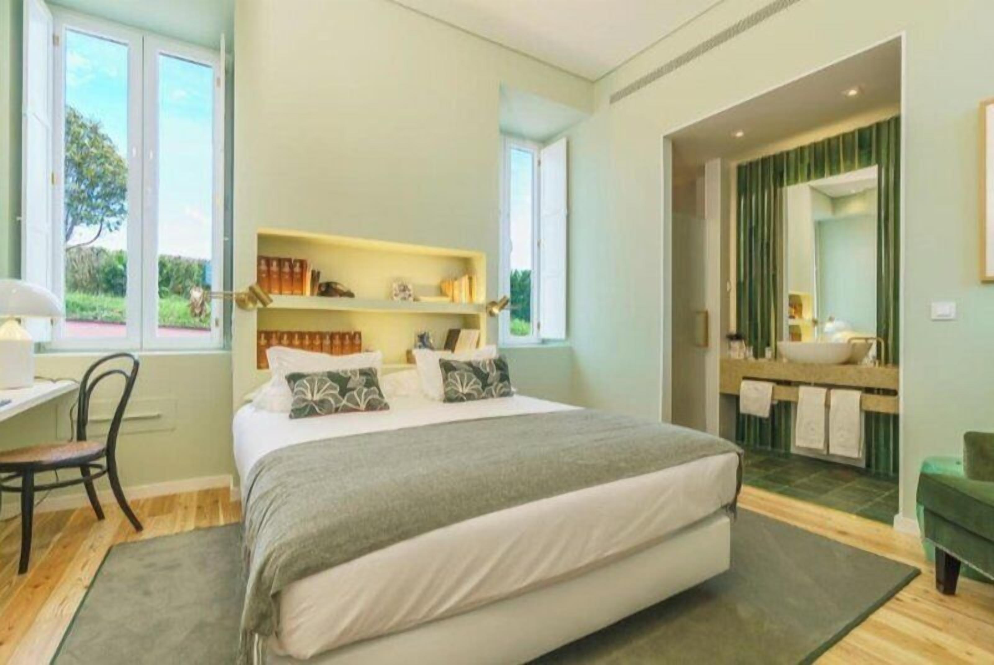A bedroom with a bed, bedside tables, a desk, and a window.