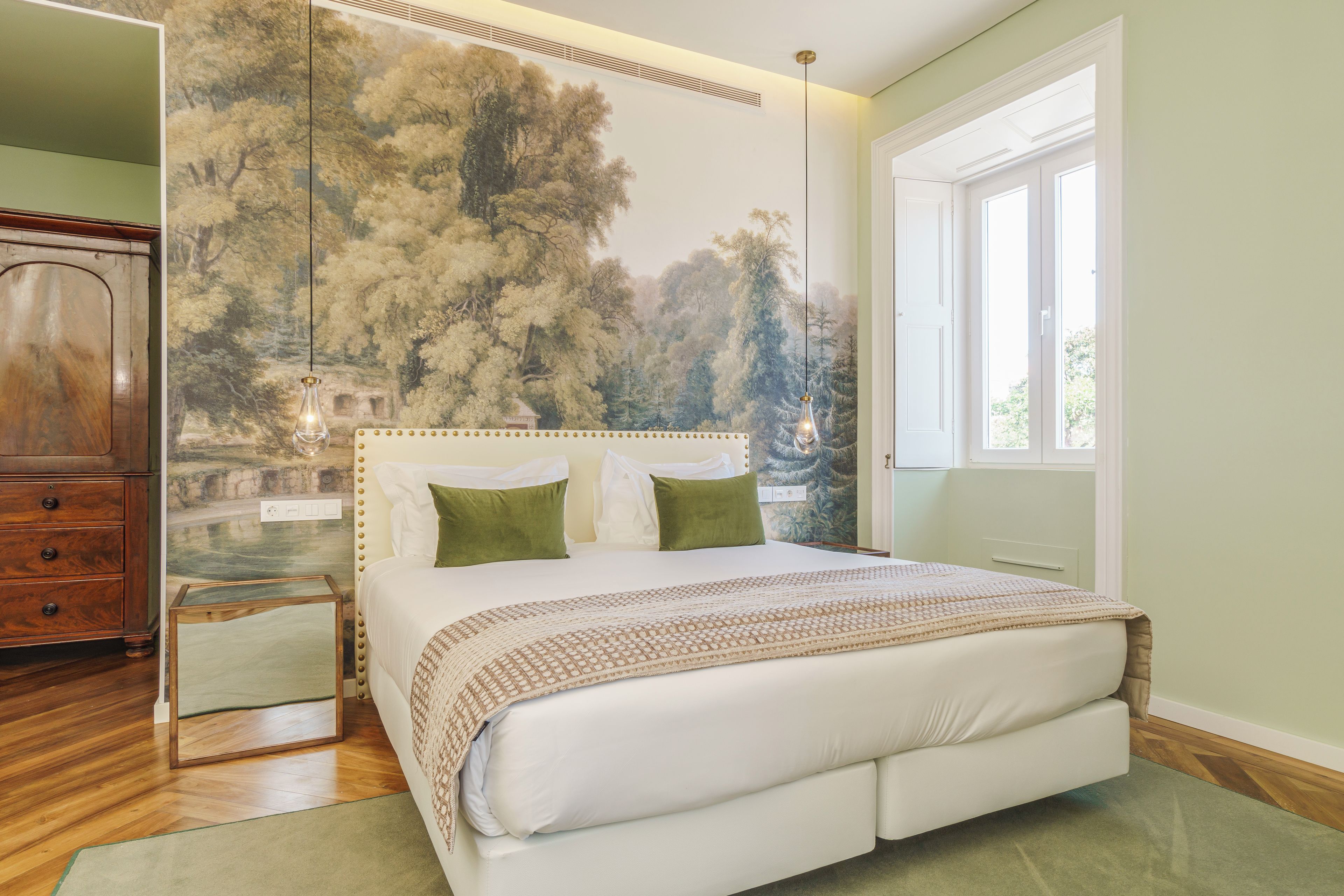 Une chambre avec un grand lit, une commode en bois et une fresque représentant des arbres sur le mur.