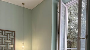 A bedroom with a bed, a nightstand, a hanging light, and a view of the outdoors through a glass door. - Solar dos Cantos Botanic House and Garden (Ponta Delgada)