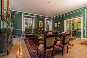 Un salón amplio con un sofá grande, dos sillones y una mesa de centro. Hay una chimenea y un espejo grande en la pared.