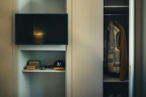 A closet with a television mounted above a shelf, containing a hat and a box.