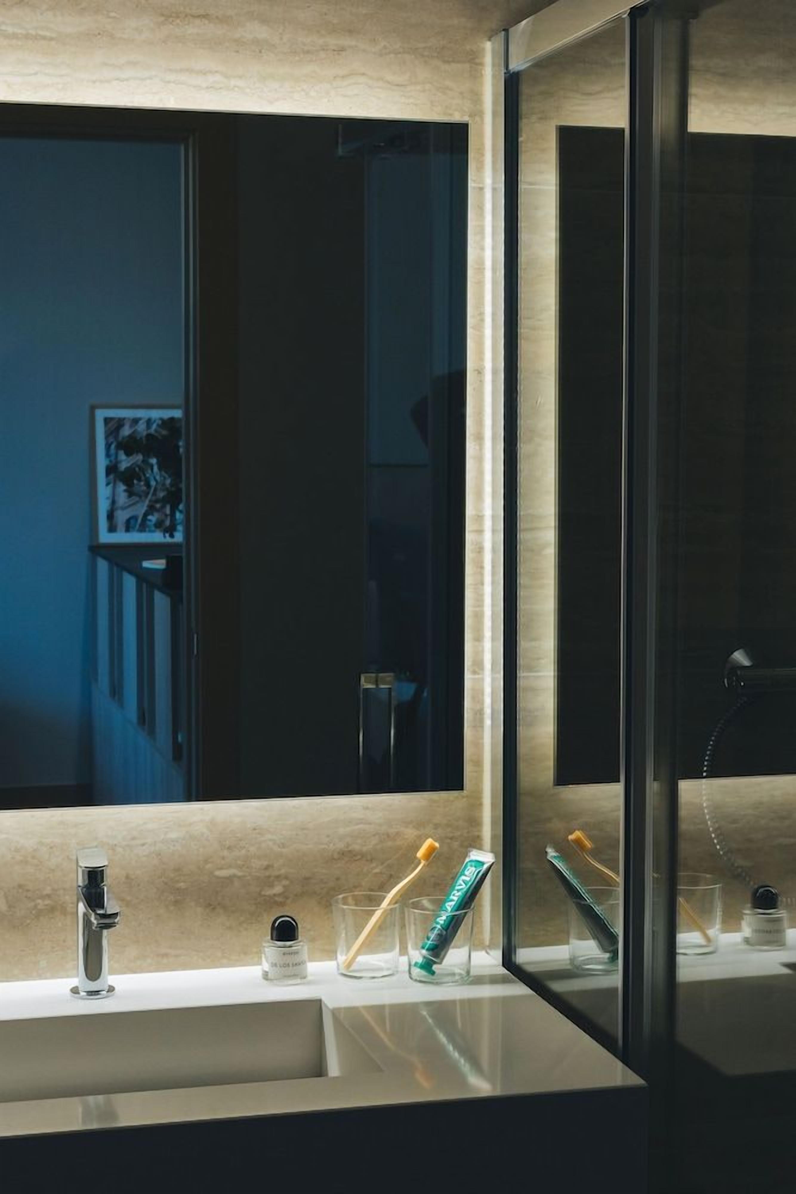 Un baño moderno con un espejo grande, un lavamanos y cepillos de dientes sobre la encimera.