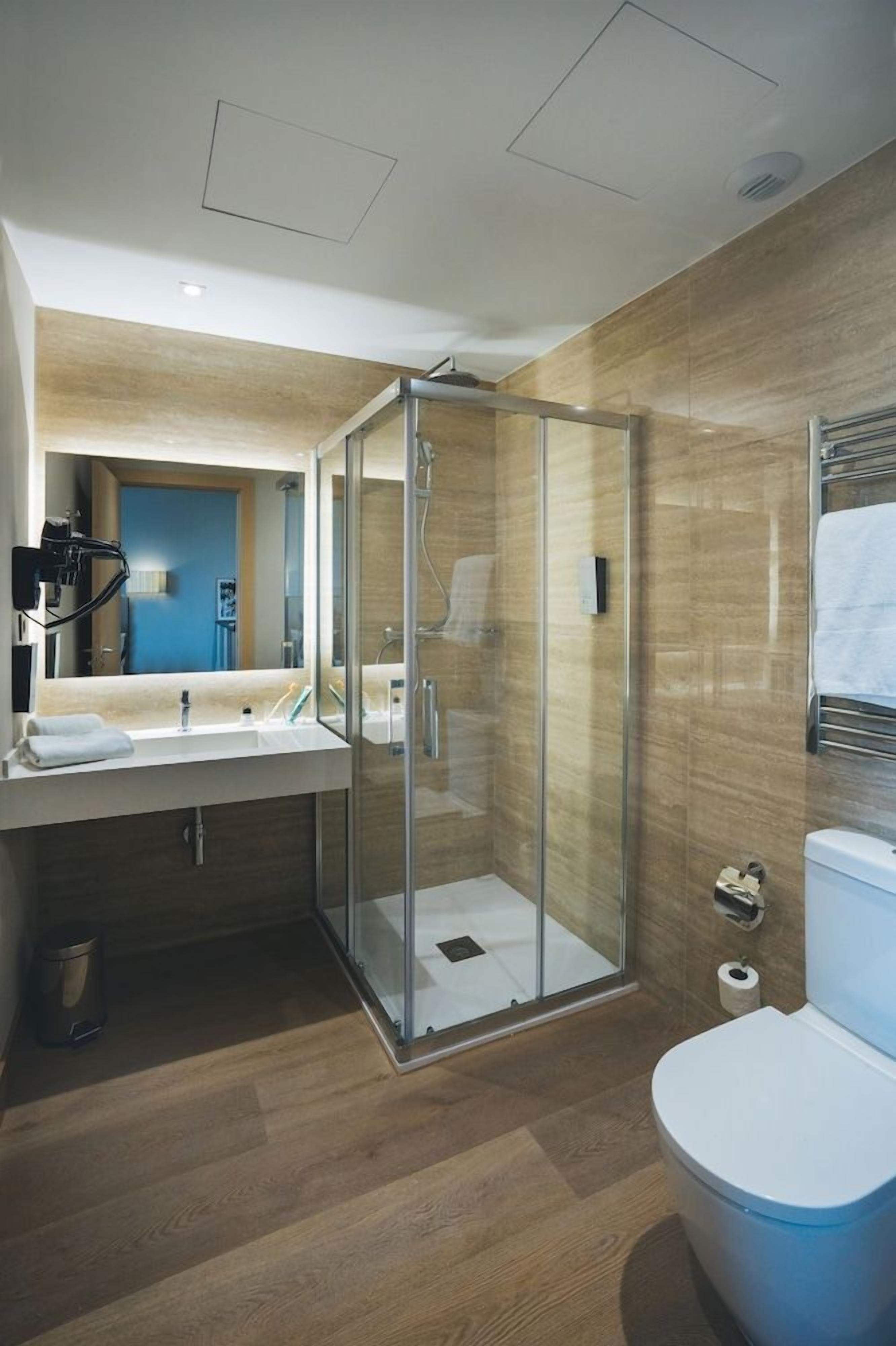 Un baño moderno con ducha envuelta en vidrio, lavamanos con espejo y retrete.
