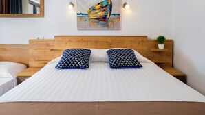 A hotel room with a wooden headboard, a large bed with white bedding, two patterned pillows, a small potted plant, and a colorful abstract painting on the wall. - D-elegant Lapad Dubrovnik (Dubrovnik)