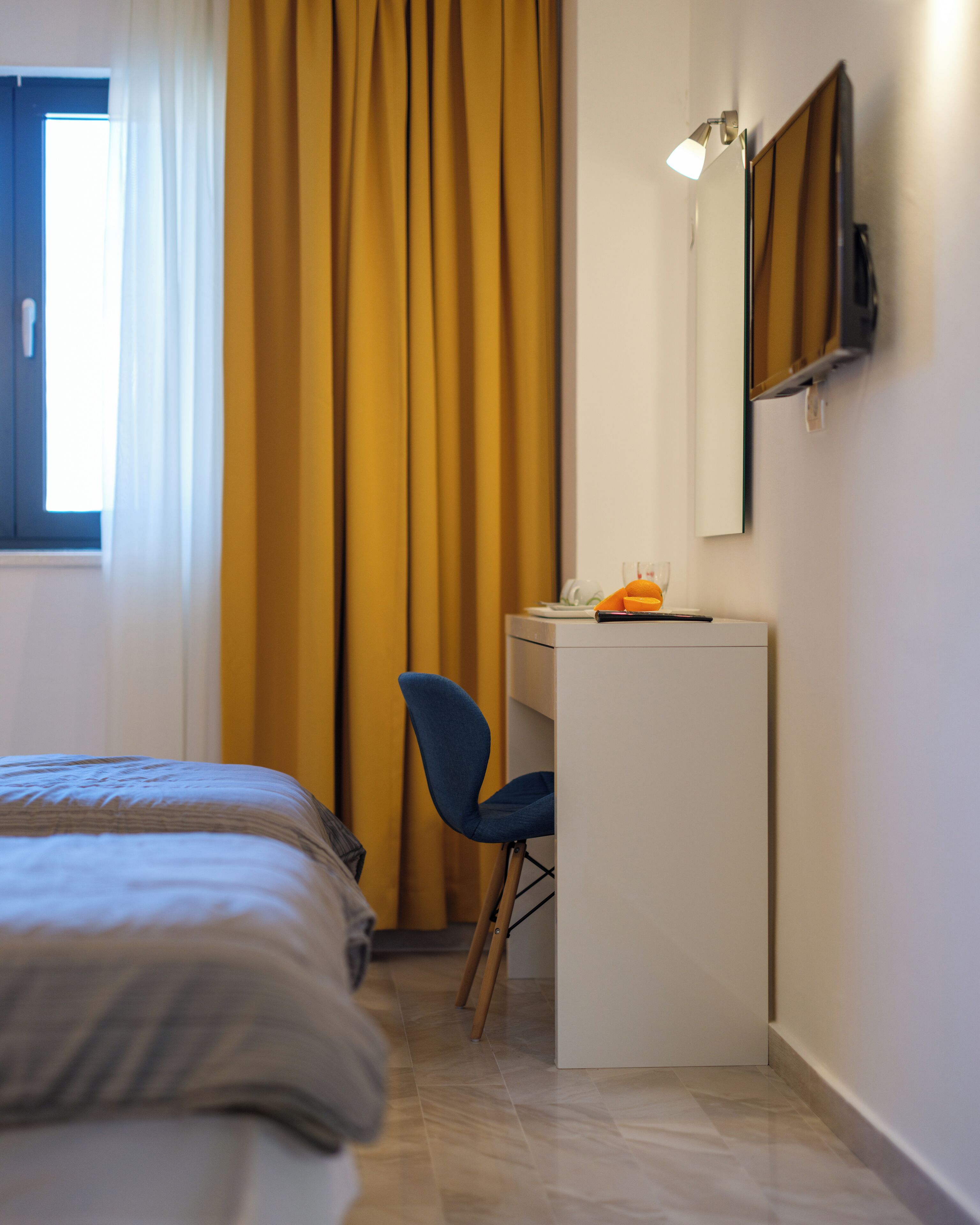 A bedroom with a bed, a desk, a chair, a mirror, and a window with curtains.