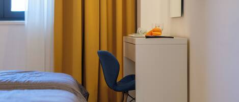 A bedroom with a bed, a desk, a chair, a mirror, and a window with curtains.