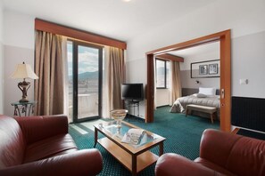 Ein Hotelzimmer mit Bett, Fernseher, Couchtisch und Blick auf die Stadt durch große Fenster.
