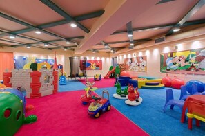 Ein Kinderspielbereich mit bunten Spielgeräten, einer Rutsche und einem großen Wandbild.