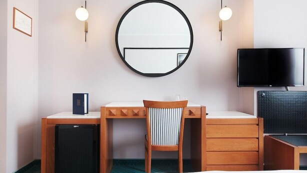 A hotel room with a round mirror, a desk with a chair, a television, and a small refrigerator. - Hotel Z Palace and Congress Center (Xanthi)