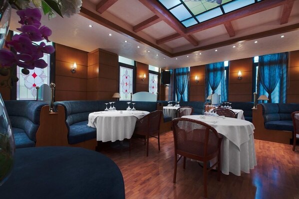 A restaurant with round tables, blue cushioned seating, and a wooden ceiling with a skylight. - Hotel Z Palace and Congress Center (Xanthi)