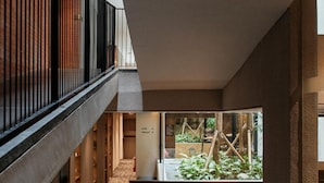 Ein mehrgeschossiges Interieur mit einer Treppe, einer Sitzecke mit Blick ins Grüne sowie einem Schild, das ein Fitnessstudio und eine Toilette kennzeichnet.