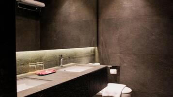 A modern bathroom with a dark marble countertop, two sinks, a toilet, and a towel rack.