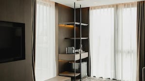 Ein modernes Hotelzimmer mit Flachbildfernseher, integrierten Regalen, einer Sitzecke mit zwei runden Tischen und großen Fenstern mit durchsichtigen Vorhängen.