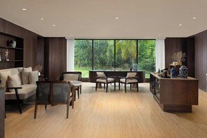 A modern living room with a sofa, two armchairs, a coffee table, and a wooden cabinet. Large windows offer a view of greenery outside. - Lampung Marriott Resort and Spa (Bandar Lampung)