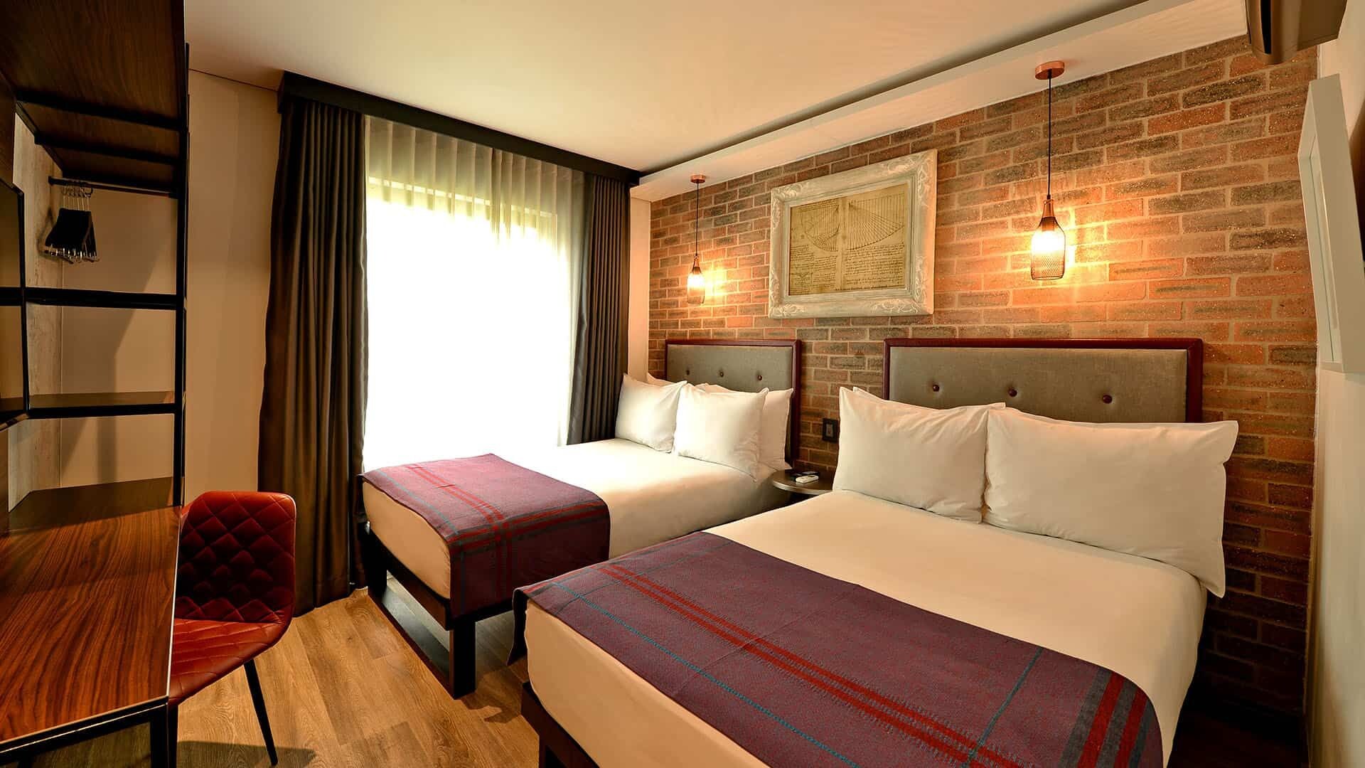 Habitación de hotel con dos camas, un escritorio, una silla y una pared de ladrillo con un cuadro enmarcado.
