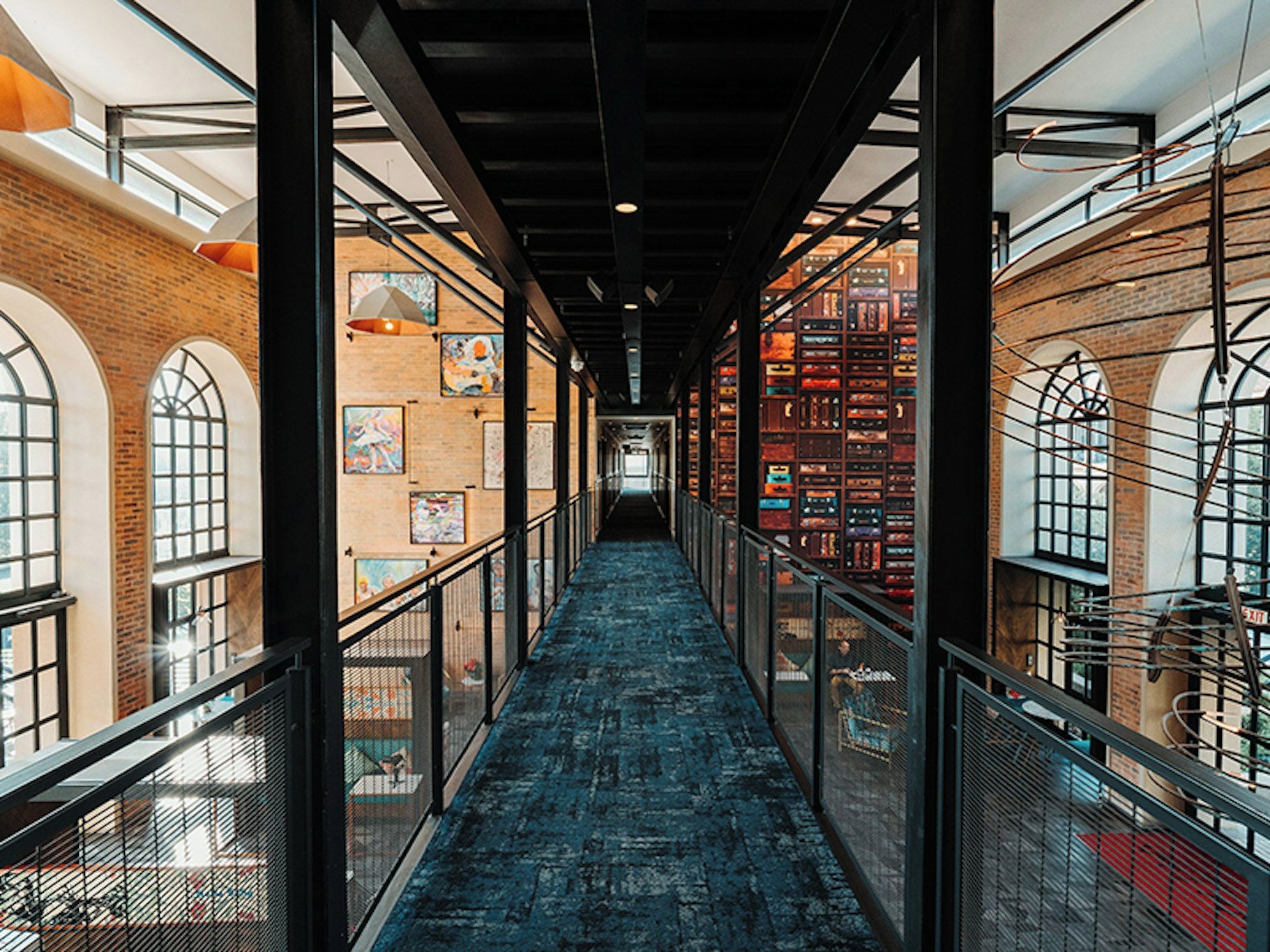 A corridor with a blue carpet, metal railings, and brick walls.