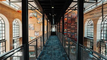 A corridor with a blue carpet, metal railings, and brick walls.