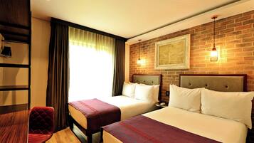 A hotel room with two beds, a wooden desk, a chair, and a brick wall with a framed picture.