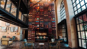 A spacious interior with a high ceiling, exposed brick walls, and a central seating area with a sofa and chairs.