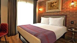 A hotel room with a bed, a red chair, a small table, and a brick wall. - Hotel Perte Montecasino (Johannesburg)