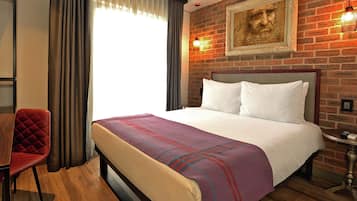 Una habitación de hotel con una cama, una silla roja, una mesita pequeña y un muro de ladrillo.