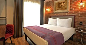 A hotel room with a bed, a red chair, a small table, and a brick wall. - Hotel Perte Montecasino (Johannesburg)
