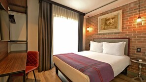 A hotel room with a bed, a desk, a chair, a window with curtains, a brick wall, and a framed picture. - Hotel Perte Montecasino (Johannesburg)
