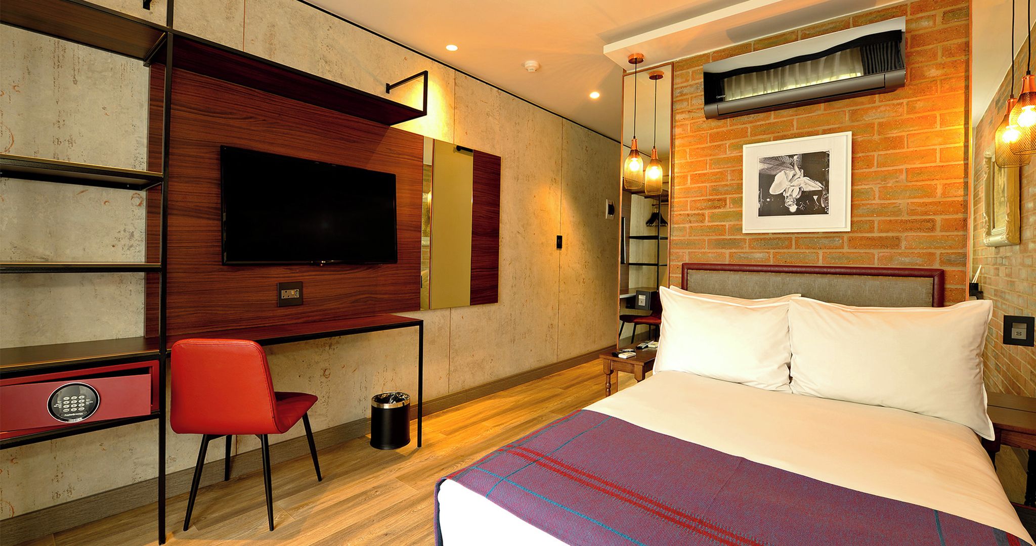 Quarto de hotel com cama, escrivaninha com cadeira, televisão e um quadro na parede.
