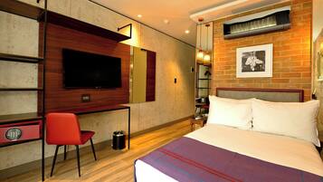 Een hotelkamer met een bed, een bureau met stoel, een televisie en een foto aan de muur.