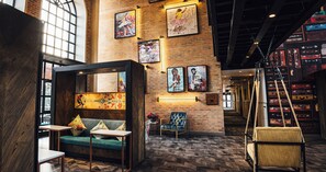 A spacious lounge area with a brick wall, a sofa, a chair, and a hanging swing. - Hotel Perte Montecasino (Johannesburg)