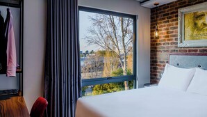 A hotel room with a large window, a bed, a wardrobe, and a brick wall.