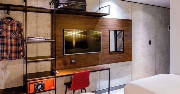 A hotel room with a wooden accent wall, a flat-screen TV, a red chair, a desk, and a bed. - Hotel Perte Montecasino (Johannesburg)