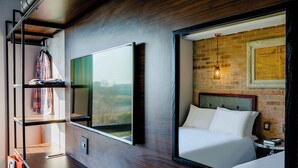 A modern hotel room with a large bed, a wardrobe, a TV, and a brick wall with a hanging light fixture. - Hotel Perte Montecasino (Johannesburg)