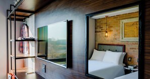 A modern hotel room with a large bed, a wardrobe, a TV, and a brick wall with a hanging light fixture. - Hotel Perte Montecasino (Johannesburg)