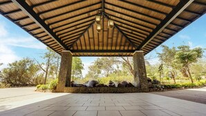 A covered pavilion with a wooden roof and stone pillars, surrounded by a landscaped garden with trees and rocks. - Club Mahindra Resort - Tungi, Lonavala, Maharashtra (Mawal)