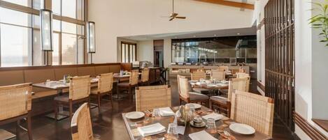 A spacious dining area with high ceilings, large windows, and modern furnishings.