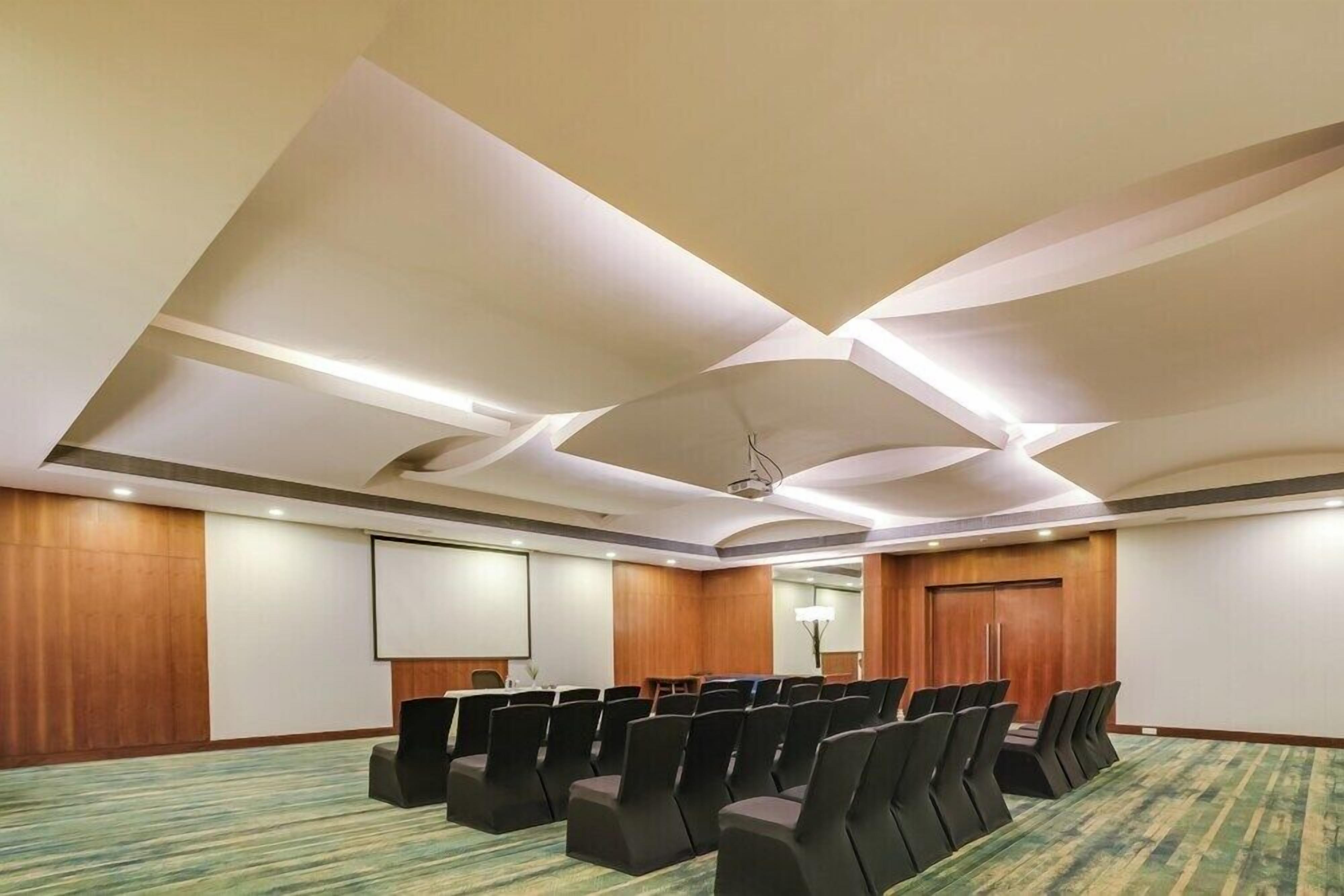 Una sala de conferencias con una pantalla grande, filas de sillas y piso alfombrado.