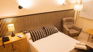 Hotelkamer met een bed, een stoel, een bureau met telefoon en lamp, en een wand met verticale houten latten.