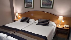 Een tweepersoonsbed met twee kussens, een nachtkastje met een lamp en een telefoon.