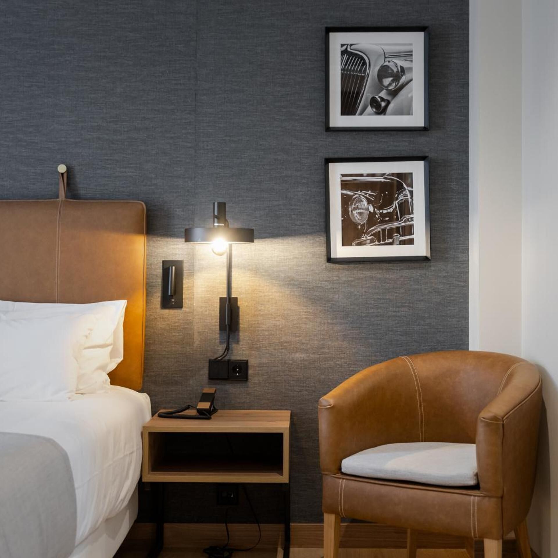 Una habitación de hotel moderna con una cama, una mesita de noche, una lámpara, una silla y dos cuadros en la pared.