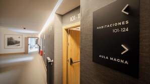 Corredor com placas de sinalização indicando os números dos quartos 101 a 124 e o nome 'AULA MAGNA'.