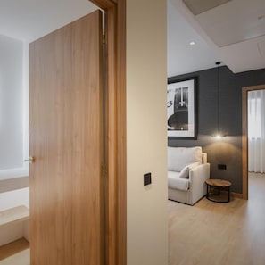 Un interior moderno con una puerta de madera, un sofá blanco, una mesita redonda y un aplique de pared.