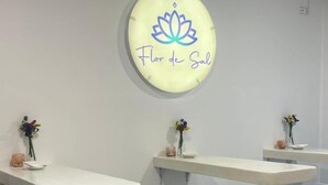 Une pièce avec des tabourets et des tables de bar blancs, un panneau mural orné d’une fleur de lotus et d’un texte, et une grille d’aération au plafond.