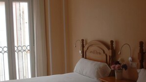 Une chambre d’hôtel avec deux lits, une fenêtre avec des rideaux, une table de chevet avec une lampe et un vase avec des fleurs.