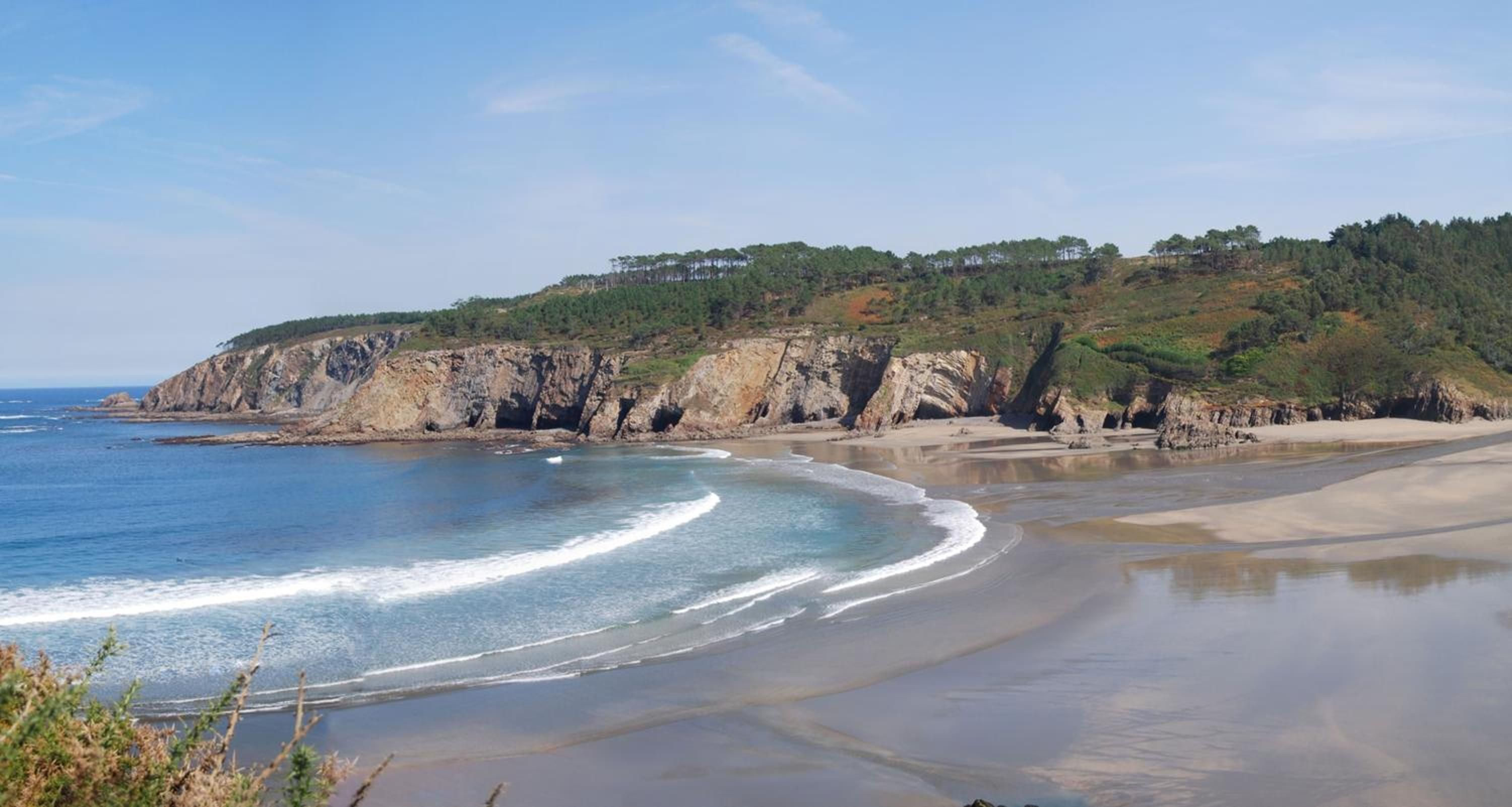 Paisatge costaner amb una platja sorrenca i penya-segades rocoses.
