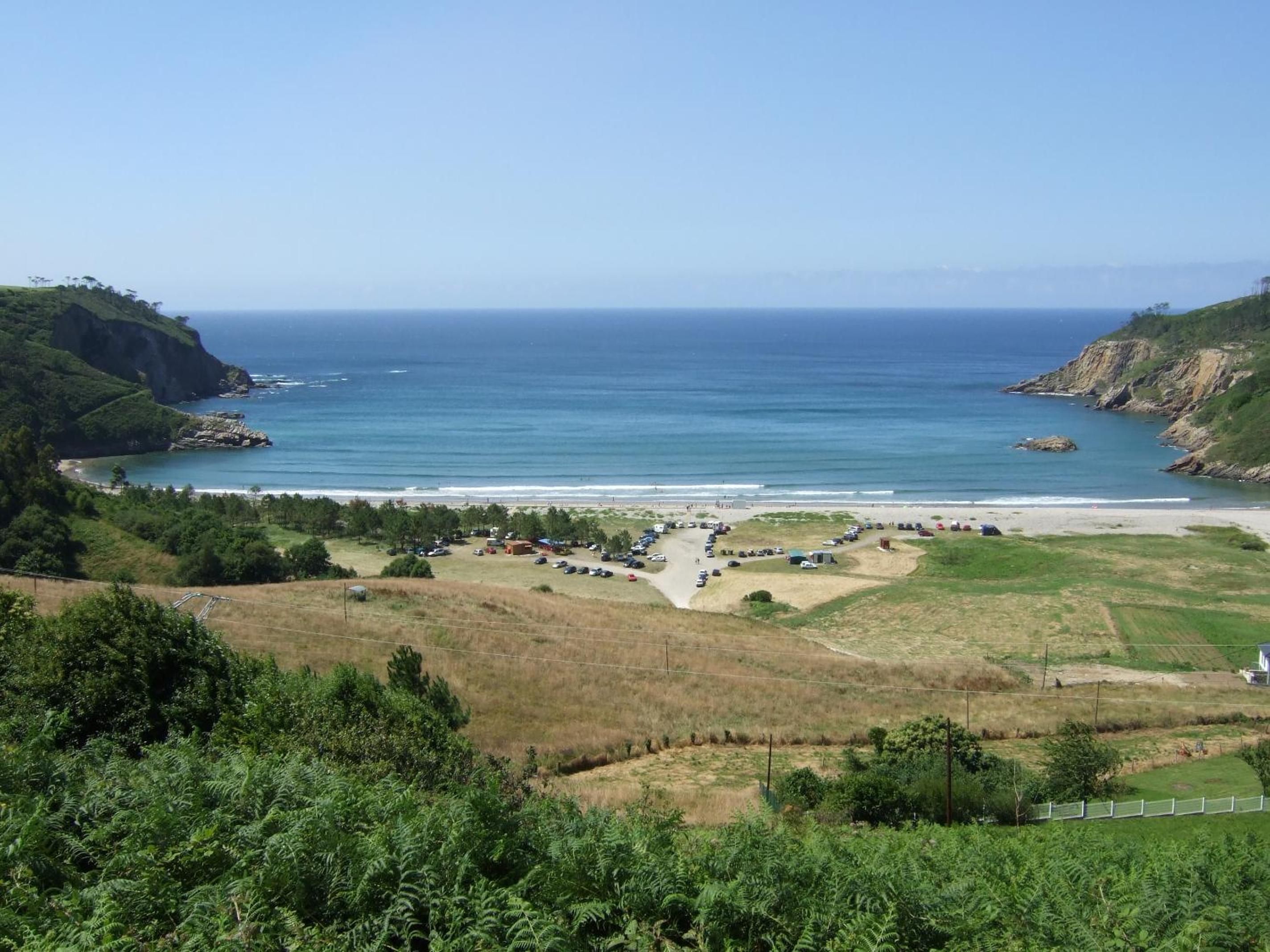 A coastal landscape with a parking area, beach, and hilly terrain.