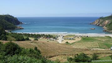 A coastal landscape with a parking area, beach, and hilly terrain.