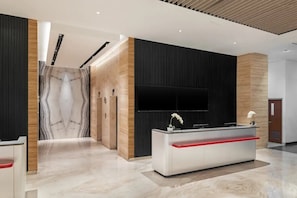 A modern reception area with a marble wall, a reception desk, and a flat-screen TV mounted on the wall. - Hotel Neo Plus Airport Jakarta (Tangerang)